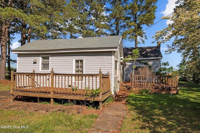 back of house with a lawn, a deck, and a shingled roof