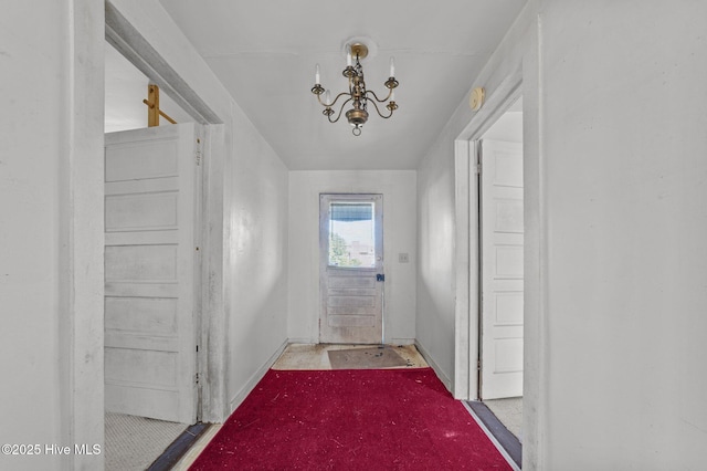 doorway featuring baseboards, a notable chandelier, and light colored carpet