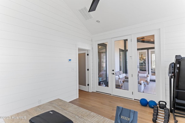 workout room with wood walls, french doors, wood finished floors, lofted ceiling, and visible vents