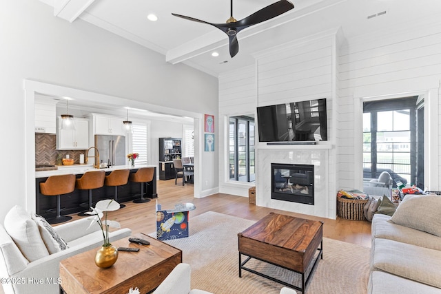 living room featuring visible vents, a fireplace, beamed ceiling, ceiling fan, and light wood-type flooring