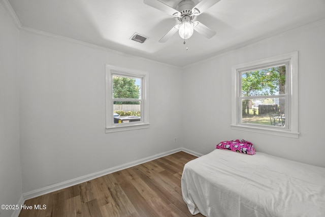 bedroom featuring a ceiling fan, visible vents, crown molding, wood finished floors, and baseboards