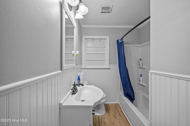 bathroom featuring shower / bath combination with curtain, crown molding, visible vents, wood finished floors, and a wainscoted wall