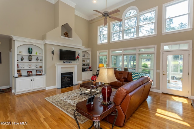 84 Deerwood Ln, Pinehurst, NC 28374 - living room featuring a high ceiling, light wood-style floors, a ceiling fan, a fireplace with flush hearth, and ornamental molding