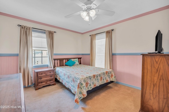 carpeted bedroom featuring a ceiling fan, wainscoting, ornamental molding, and multiple windows