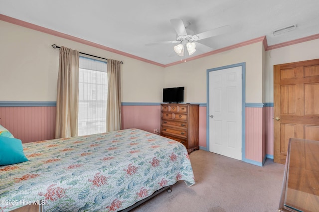 carpeted bedroom with visible vents, crown molding, a wainscoted wall, and ceiling fan