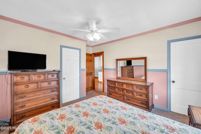 carpeted bedroom featuring baseboards, ornamental molding, a ceiling fan, and a wainscoted wall