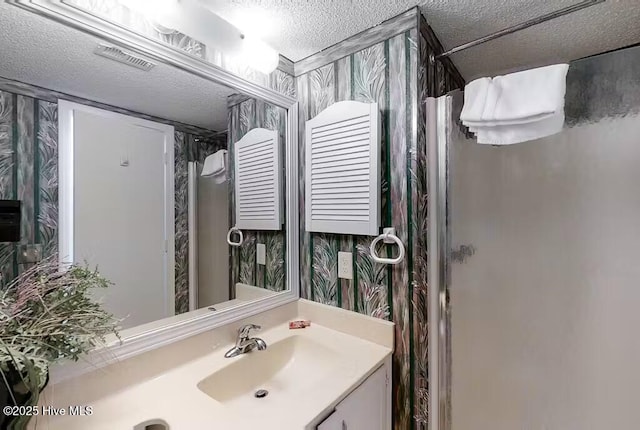 bathroom featuring a textured ceiling, visible vents, a shower, vanity, and wallpapered walls