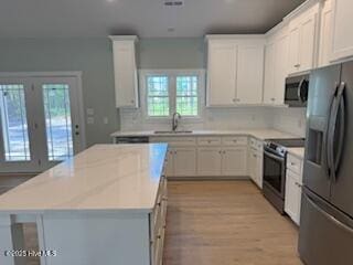 kitchen with a kitchen island, light countertops, a sink, backsplash, and stainless steel appliances