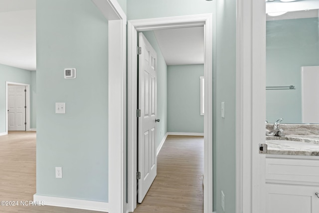 hall with baseboards, a sink, and light wood-style flooring