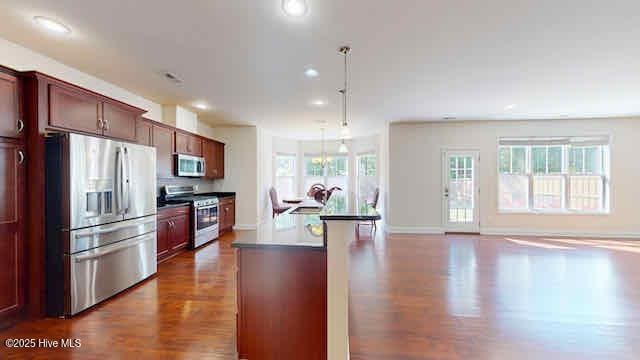 kitchen featuring hanging light fixtures, dark wood-type flooring, stainless steel appliances, recessed lighting, and an island with sink