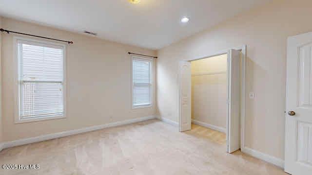unfurnished bedroom featuring baseboards, carpet, lofted ceiling, and multiple windows