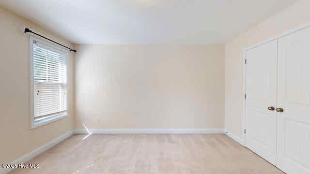 unfurnished bedroom featuring baseboards, light carpet, and a closet