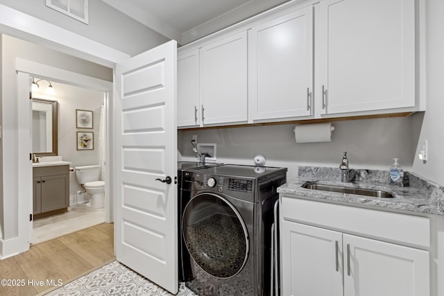laundry area with cabinet space, a sink, light wood finished floors, washer / clothes dryer, and visible vents
