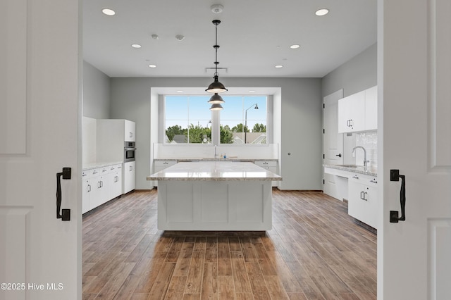 kitchen with a kitchen island, light wood-type flooring, white cabinets, tasteful backsplash, and a sink