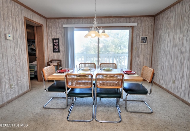 carpeted dining room with crown molding, baseboards, and wood walls