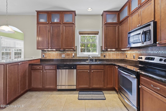 kitchen featuring a sink, dark stone counters, stainless steel appliances, light tile patterned floors, and backsplash