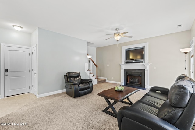 living area with light colored carpet, a ceiling fan, baseboards, a fireplace with flush hearth, and stairway