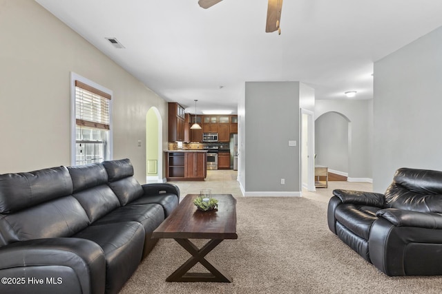 living area featuring arched walkways, ceiling fan, visible vents, and light carpet