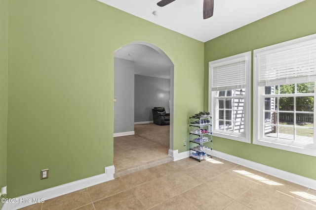 empty room featuring tile patterned flooring, arched walkways, baseboards, and ceiling fan