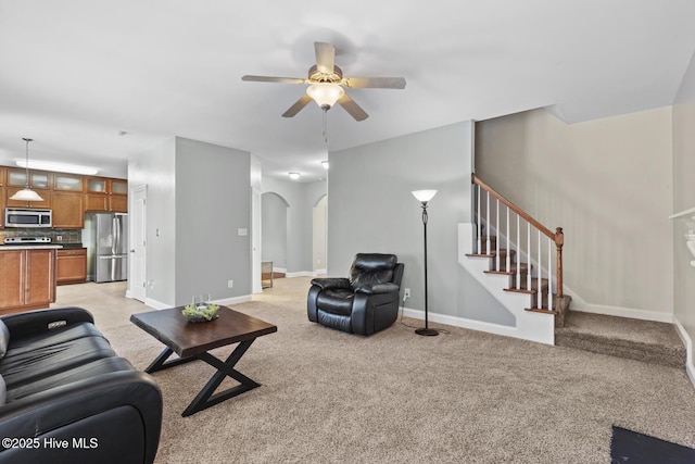 living room with light carpet, arched walkways, a ceiling fan, baseboards, and stairway