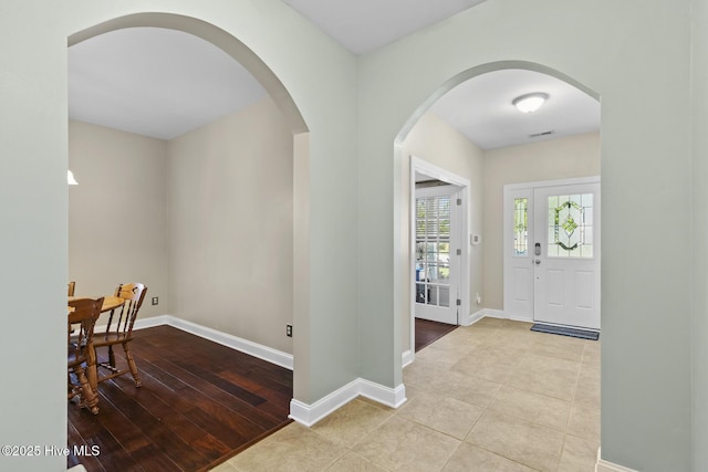 entryway featuring arched walkways, baseboards, and tile patterned flooring