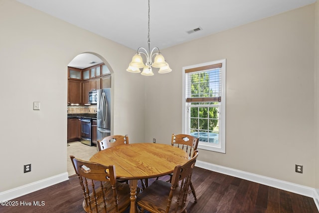 dining room featuring a notable chandelier, arched walkways, baseboards, wood finished floors, and visible vents