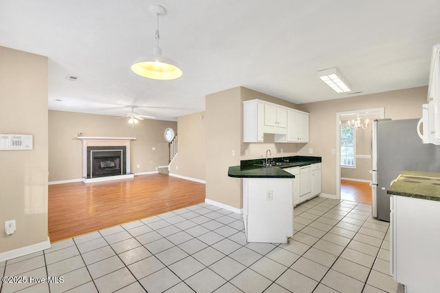 kitchen featuring light tile patterned floors, dark countertops, white cabinets, and ceiling fan with notable chandelier