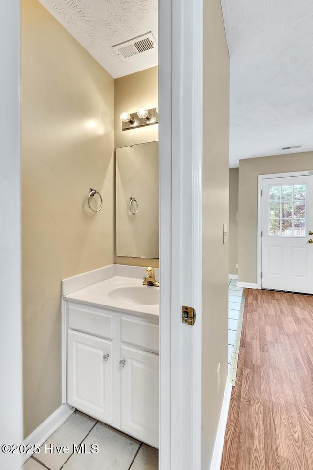 bathroom with baseboards, vanity, a textured ceiling, and visible vents
