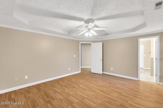 spare room with a ceiling fan, visible vents, light wood-style flooring, and a raised ceiling