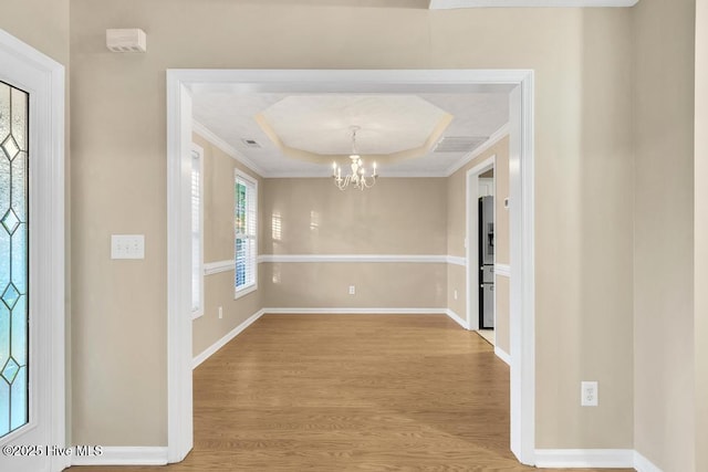 interior space featuring ornamental molding, a raised ceiling, light wood finished floors, and a notable chandelier