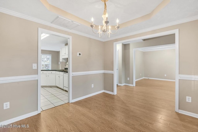 empty room with a raised ceiling, light wood finished floors, a chandelier, baseboards, and visible vents
