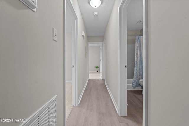 corridor featuring light wood-style floors, baseboards, a textured ceiling, and visible vents