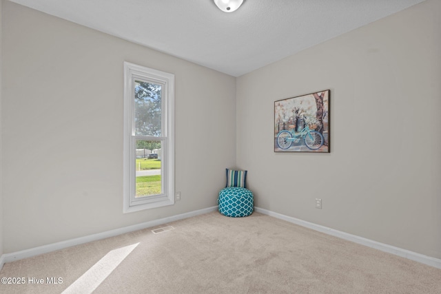 carpeted spare room featuring baseboards, plenty of natural light, and visible vents