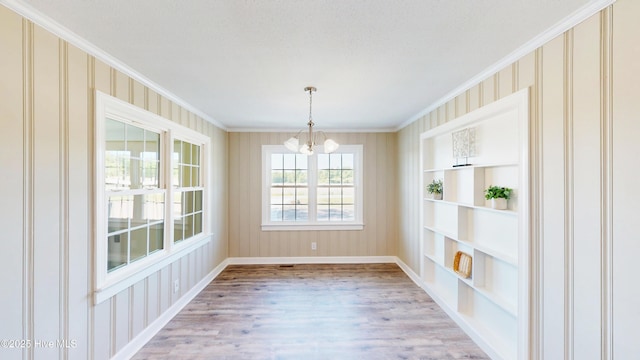 unfurnished dining area featuring a chandelier, light wood-style floors, crown molding, baseboards, and built in features