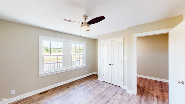 unfurnished bedroom featuring wood finished floors, a closet, baseboards, and ceiling fan