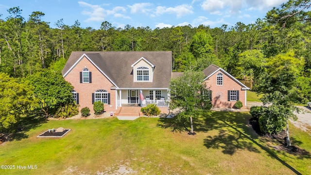 view of front of property featuring a porch, brick siding, a front yard, and a forest view