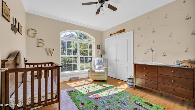 bedroom with ornamental molding, light wood-style flooring, a ceiling fan, and a crib