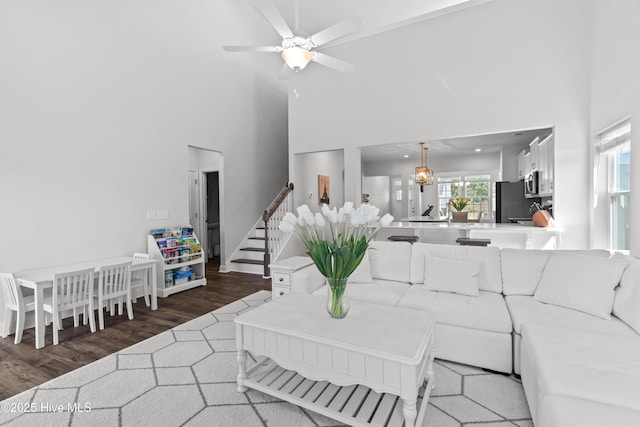 living area with ceiling fan, wood finished floors, stairway, and a towering ceiling