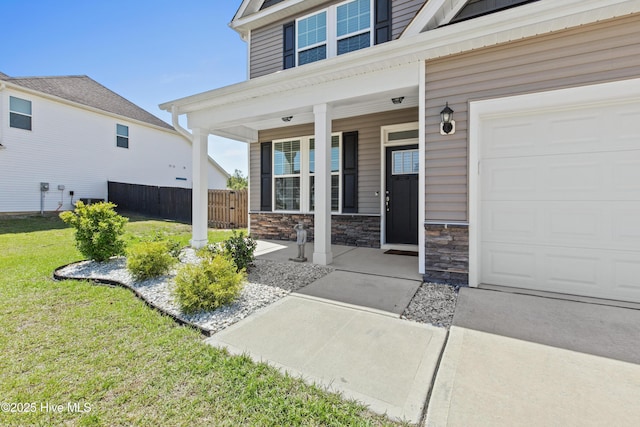 property entrance featuring a garage, fence, covered porch, stone siding, and a lawn