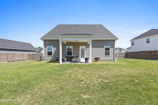 rear view of house featuring a fenced backyard, a patio, a shingled roof, and a yard