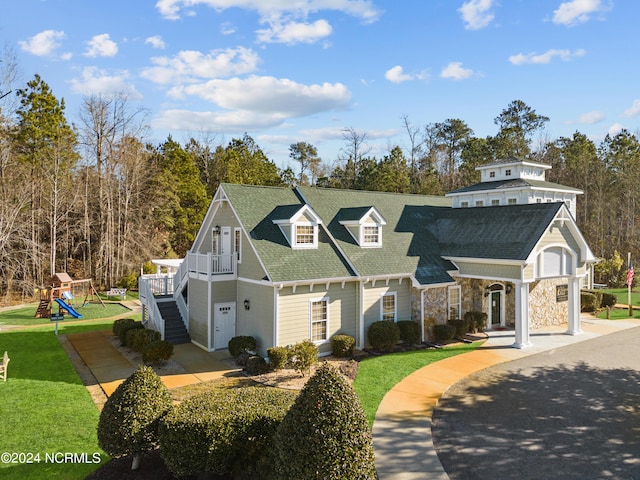 view of front of house featuring stone siding, a front yard, a shingled roof, a playground, and stairway