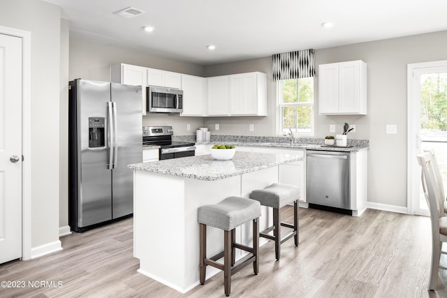 kitchen with light wood-style floors, appliances with stainless steel finishes, a kitchen island, and white cabinetry