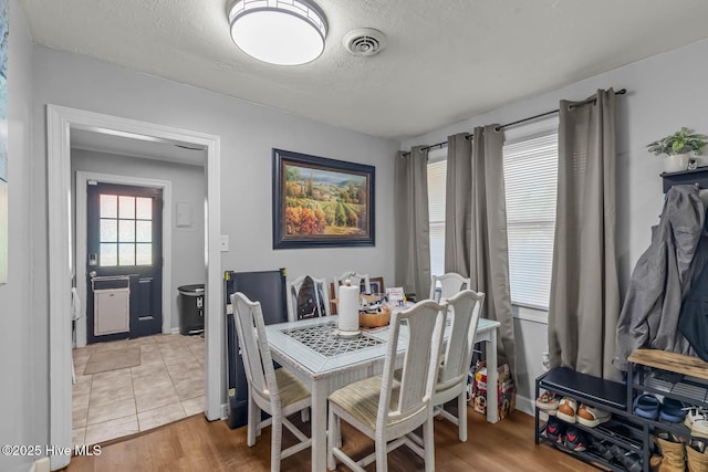 dining area with light wood-style floors, a textured ceiling, and visible vents