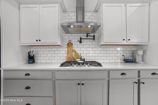 kitchen featuring decorative backsplash, wall chimney exhaust hood, stainless steel gas cooktop, and white cabinetry