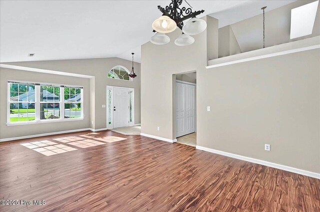 unfurnished living room with baseboards, a notable chandelier, and wood finished floors
