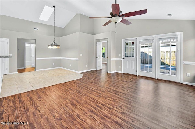 unfurnished living room with a healthy amount of sunlight, a skylight, ceiling fan with notable chandelier, and wood finished floors