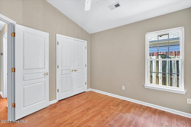 unfurnished bedroom featuring light wood finished floors, baseboards, lofted ceiling, visible vents, and a closet