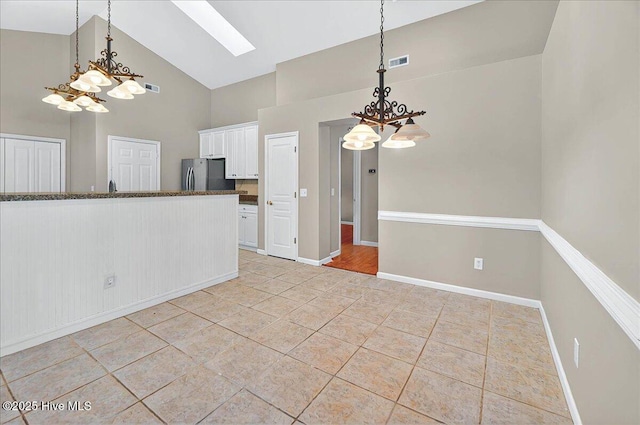 interior space featuring an inviting chandelier, freestanding refrigerator, visible vents, high vaulted ceiling, and white cabinetry