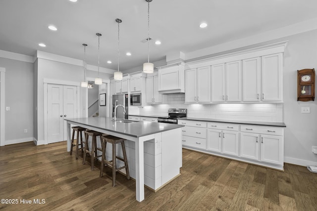 kitchen featuring decorative backsplash, dark countertops, an island with sink, white cabinets, and stainless steel appliances