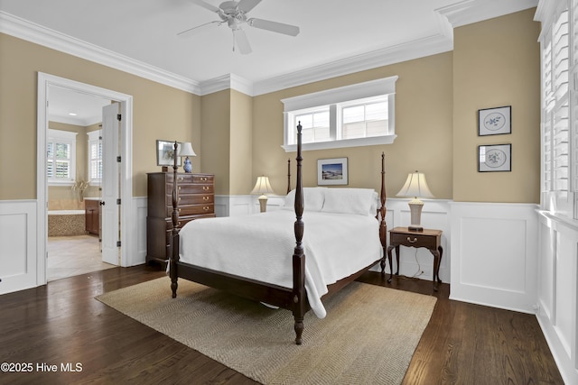 bedroom featuring crown molding, wood finished floors, a wainscoted wall, a ceiling fan, and ensuite bath